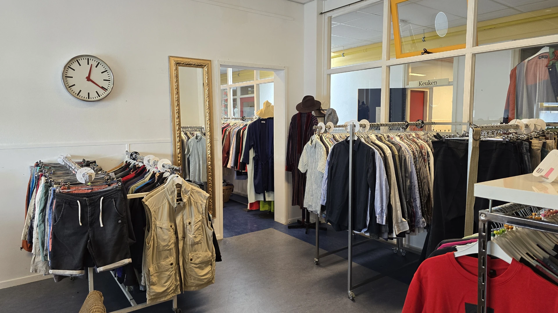 Winkelinterieur met kledingrekken vol tweedehands kleding, spiegel en klok aan de muur