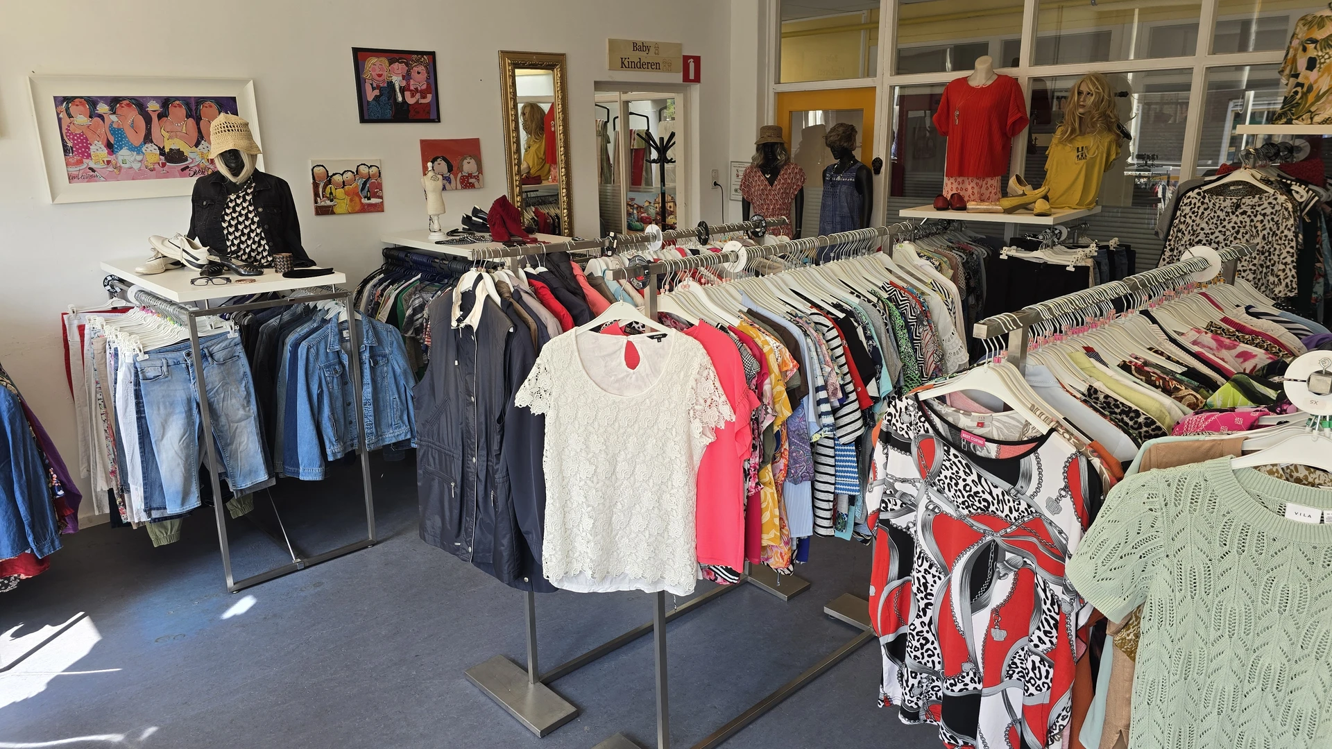 Rekken met tweedehands kleding, voornamelijk t-shirts en tops in verschillende kleuren, uitgestald in de winkel