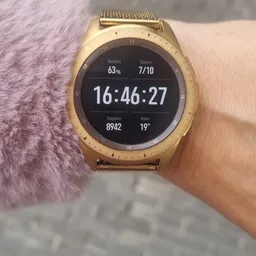 Goudkleurig smartwatch aan de pols met scherm waarop tijd en gezondheidsgegevens worden weergegeven