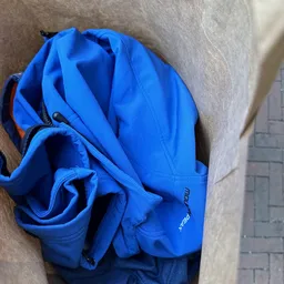 Blauwe opgevouwen jas of jack met rood accent op de mouw, op grijze ondergrond