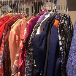 Rekken met kleding in verschillende kleuren, waaronder rode, paarse, zwarte en blauwe kledingstukken op hangers