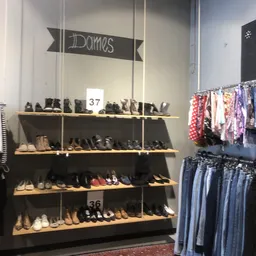 Schoenensortiment op houten schappen met nummering, kleding aan rekken ernaast