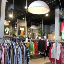 Winkelinterieur met kledingrekken vol tweedehands kleding, hangende lampen en etalagepoppen met outfits