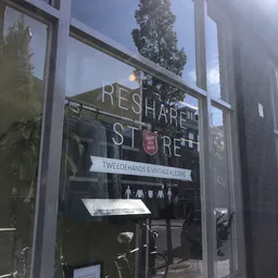Glazen winkelpui met witte letters 'RESHARETORE' en onderbord 'TWEEDEHANKS & VINTAGE KLEDING'