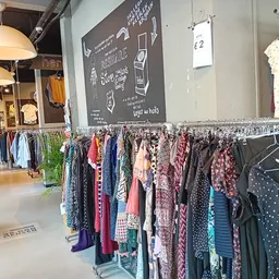 Winkelinterieur met rekken vol tweedehands kleding, hangende lampen en een krijtbord aan de muur