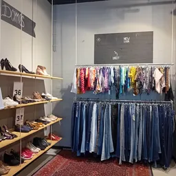 Winkelinterieur met schoenenstelage links en rekken met kleding, waaronder jeans en gekleurde kledingstukken rechts