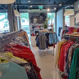 Winkelvloer met rekken vol tweedehands kleding in verschillende kleuren, stoelen en decoratie op de achtergrond