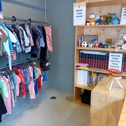 Winkelinterieur met kledingrekken links en houten boekenkasten rechts met speelgoed en gratis items