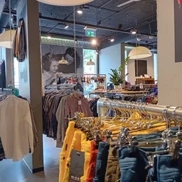 Winkelvloer met kledingrekken vol tweedehands kleding op gele hangers, kolommen, verlichting en groene muur