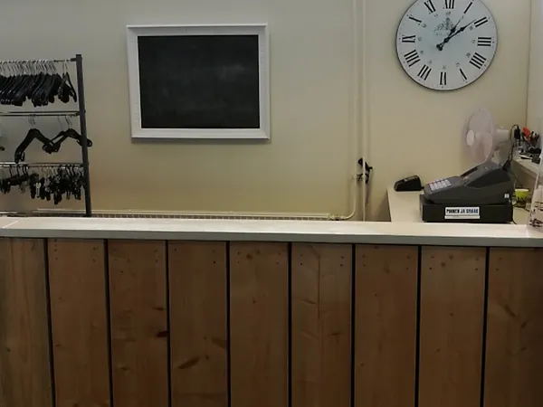 Binnenkant van kledingkringloop met toonbank, klok aan muur en kledingrekken op achtergrond