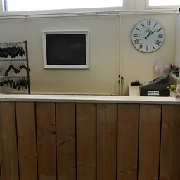 Binnenaanzicht van een kledingkringloop met toonbank, rekken met kleding, klok en zwart bord