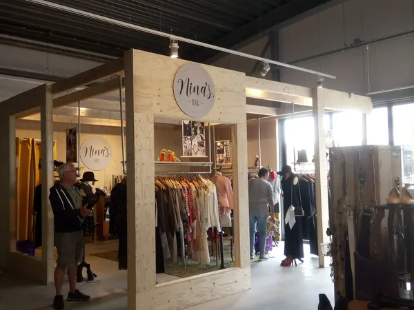 Winkelinterieur met houten stellingen vol kleding, klanten aan het winkelen, moderne kringloopwinkel