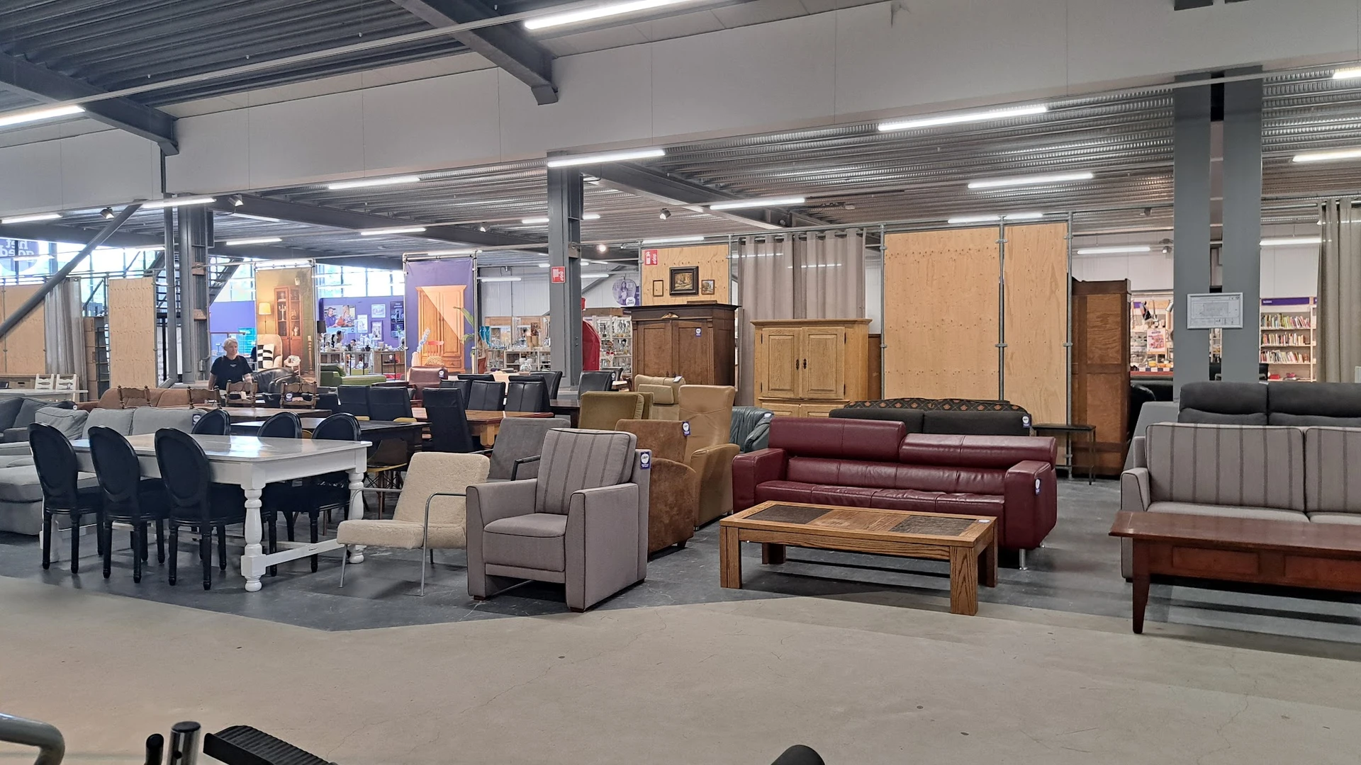 Winkelvloer met meubels: grijze fauteuils, bordeauxrode bank, houten salontafel en houten kasten tegen de muur