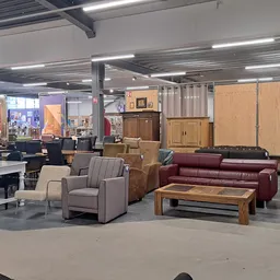 Winkelvloer met meubels: grijze fauteuils, bordeauxrode bank, houten salontafel en houten kasten tegen de muur