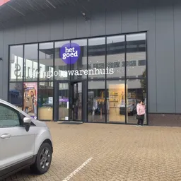 Gevel van kringloopwinkel met grote ramen, blauwe 'het goed' logo en 'Kringloopwarenhuis' tekst zichtbaar