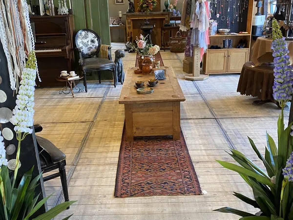 Winkelvloer met houten tafel, stellingen met kleding, decoratieve bloemen en meubilair