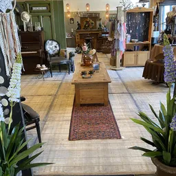 Winkelvloer met houten tafel, stellingen met kleding, decoratieve bloemen en meubilair