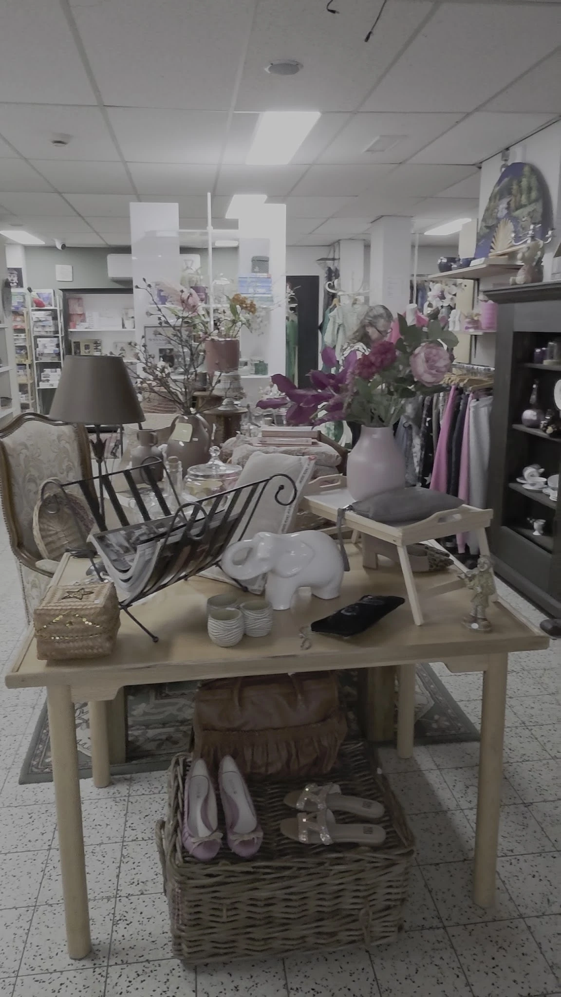 Uitgestalde meubels en decoratie-items in een kringloopwinkel, waaronder stoelen, lampen, vazen en bloemen