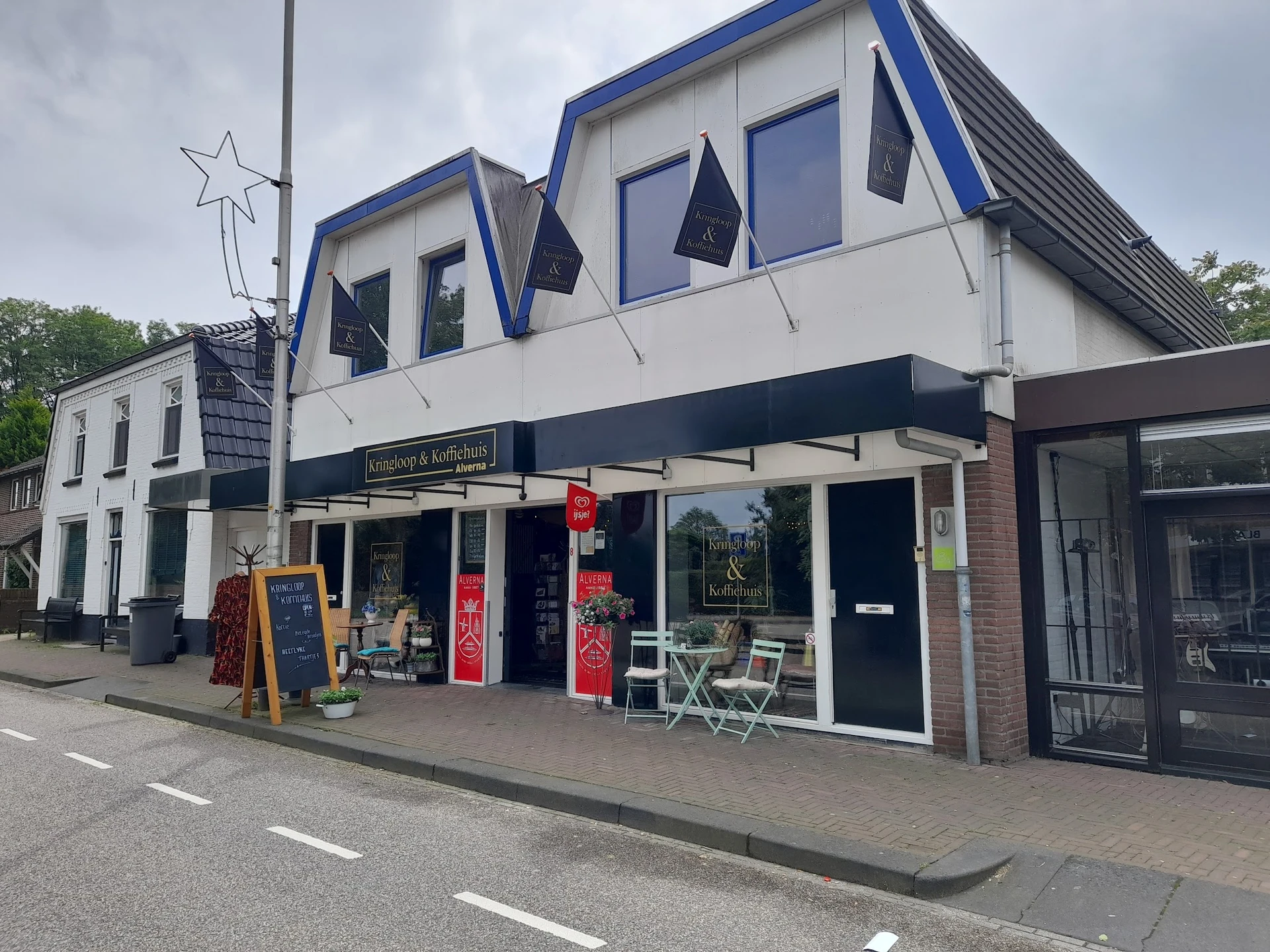 Witte winkelgevel met blauwe accenten en grote ramen, met terras en rode decoratie aan de voorkant