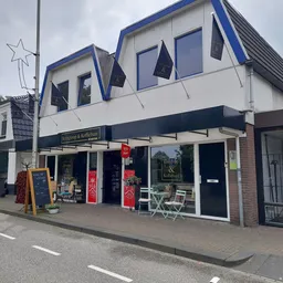 Witte winkelgevel met blauwe accenten en grote ramen, met terras en rode decoratie aan de voorkant