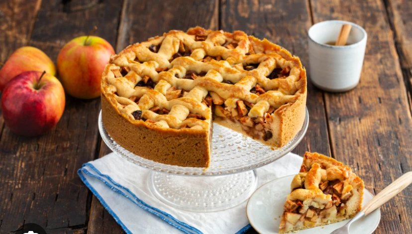 Appeltaart op een taartschep met een stuk op een bordje, appels en een kopje op houten achtergrond