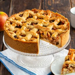 Appeltaart op een taartschep met een stuk op een bordje, appels en een kopje op houten achtergrond