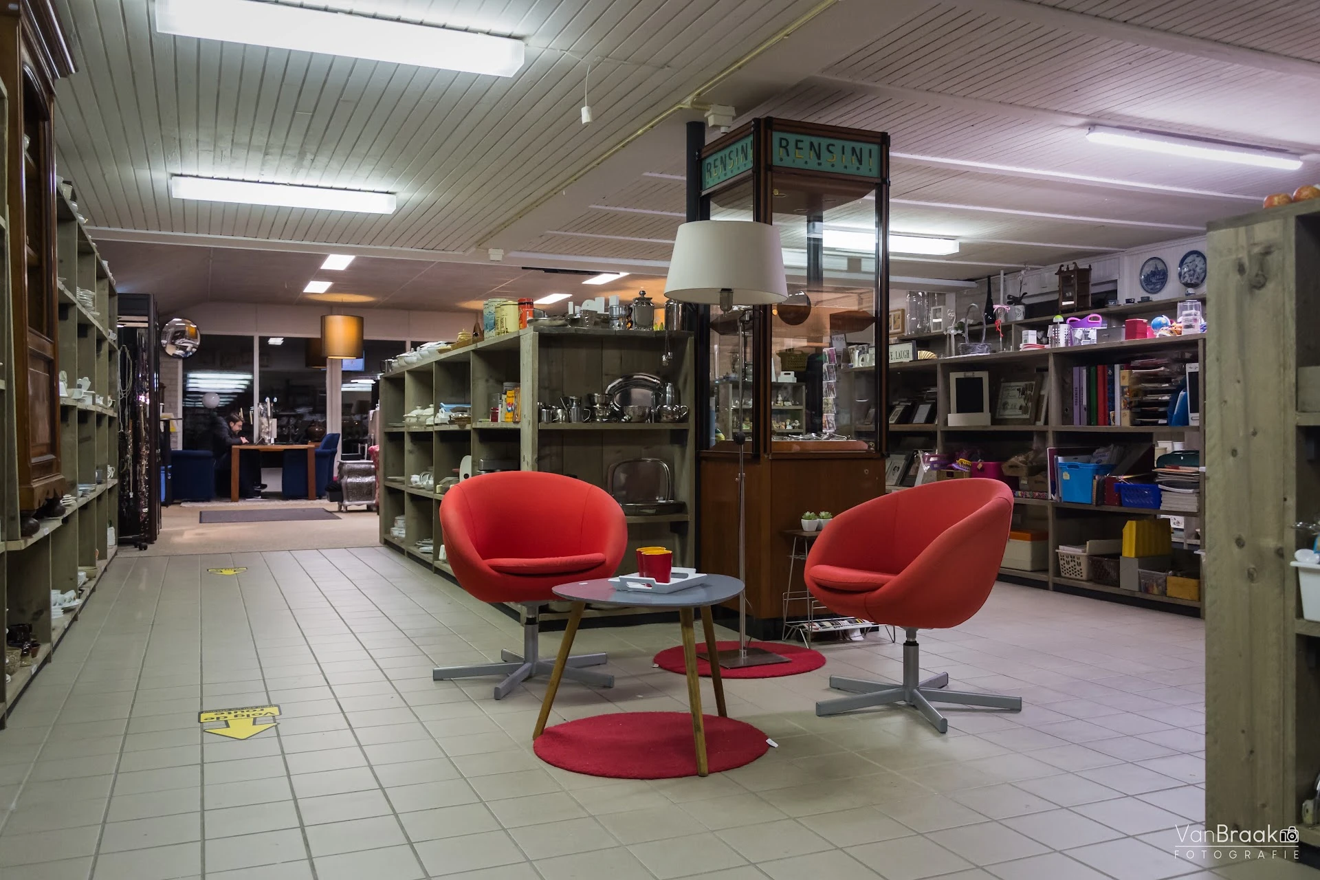Winkelvloer met twee rode stoelen rond een lage tafel, omgeven door kastenwanden met diverse spullen