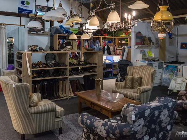 Zithoek met vintage stoelen en hangende lampen in kringloopwinkel met boekenkasten en displays op achtergrond