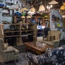 Zithoek met vintage stoelen en hangende lampen in kringloopwinkel met boekenkasten en displays op achtergrond