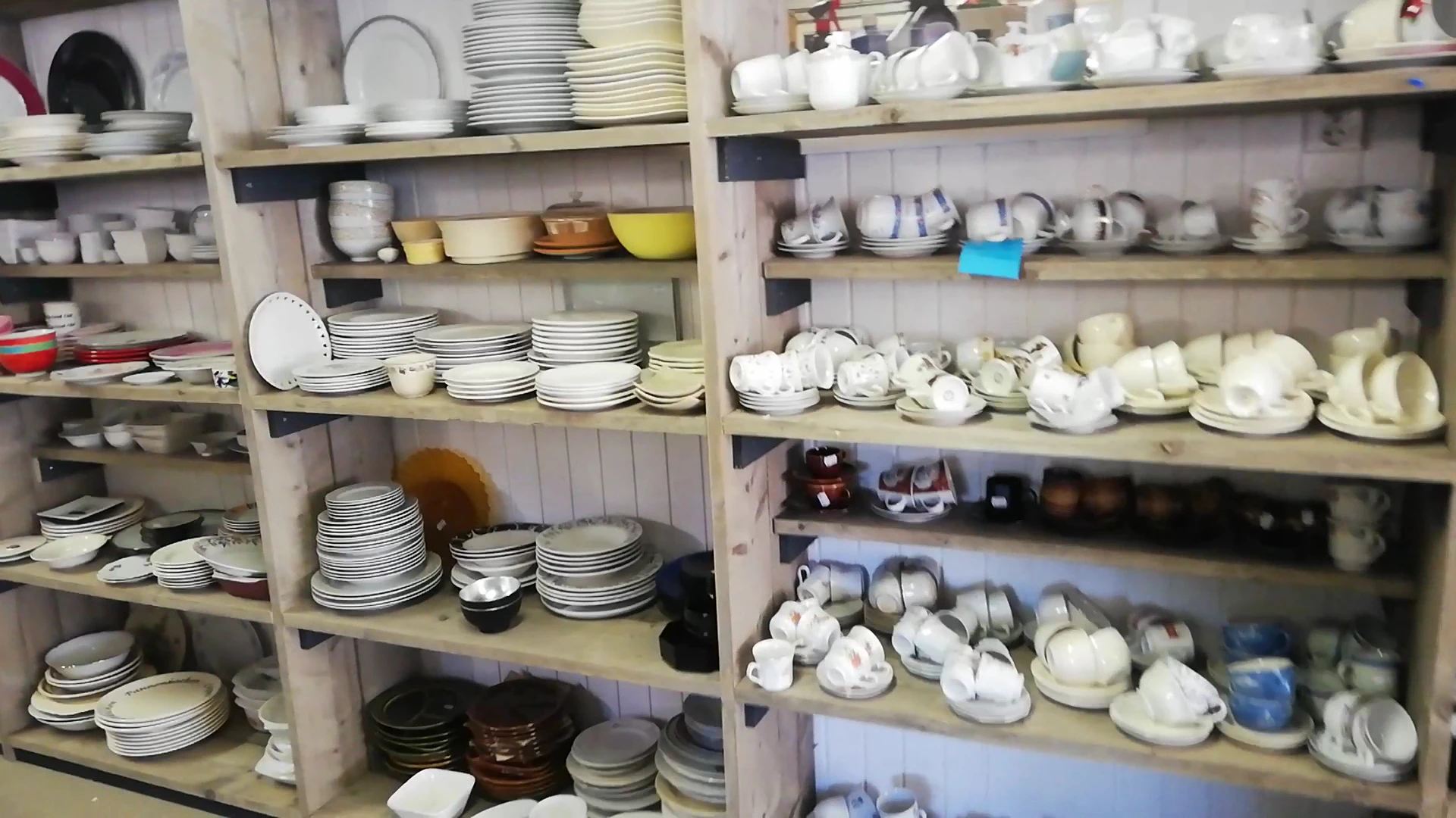 Stellingen vol met wit en crèmekleurig serviesgoed, borden, kopjes en schalen in een kringloopwinkel