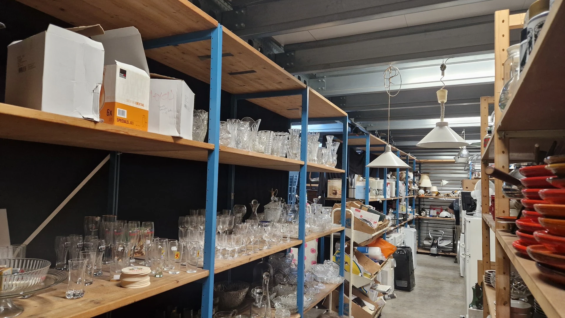 Stellingen met glazen, vazen en serviesgoed in een kringloopwinkel