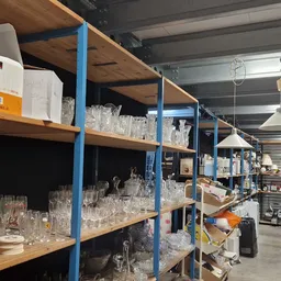 Stellingen met glazen, vazen en serviesgoed in een kringloopwinkel