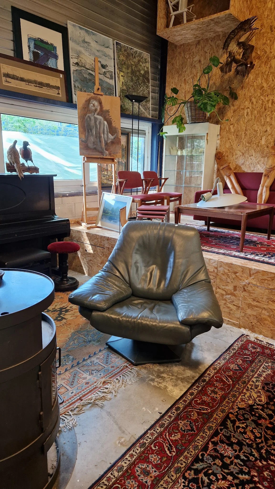 Woonkamer met zwarte leren fauteuil, piano, rode stoelen en houten meubels