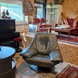 Woonkamer met zwarte leren fauteuil, piano, rode stoelen en houten meubels
