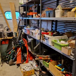 Werkplaats of opslagruimte met metalen stellingen vol dozen, gereedschap en diverse spullen