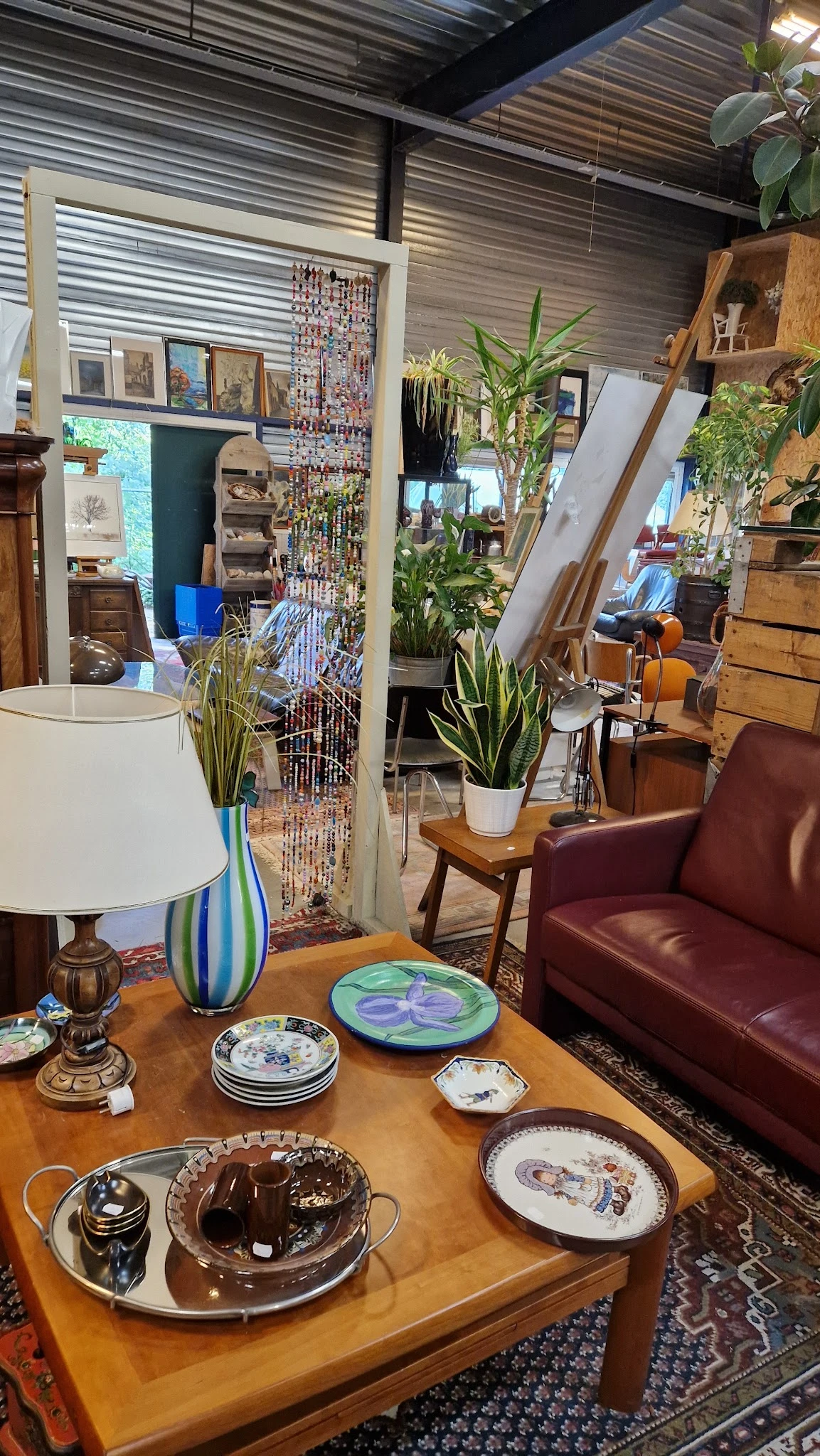 Winkelbinnenruimte met zithoek met bordeauxrood leren fauteuil, houttafel, plantendecoratie en lamp, met stellingen en items 