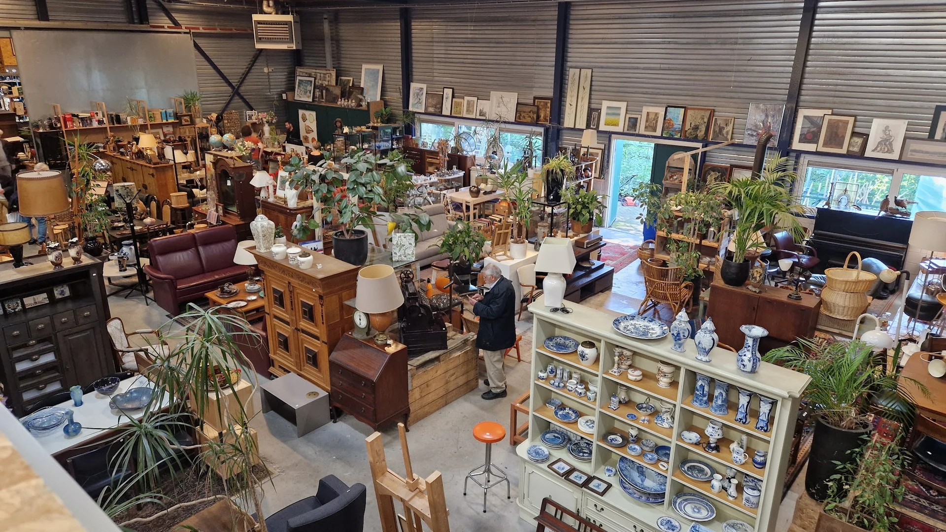 Overzicht van kringloopwinkel met meubels, huishoudwaar, plantenbakken en diverse spullen uitgestald op meerdere niveaus
