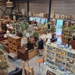 Overzicht van kringloopwinkel met meubels, huishoudwaar, plantenbakken en diverse spullen uitgestald op meerdere niveaus