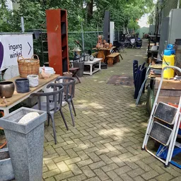 Overdekt terras met tafels, stoelen en diverse spullen in een kringloopwinkel