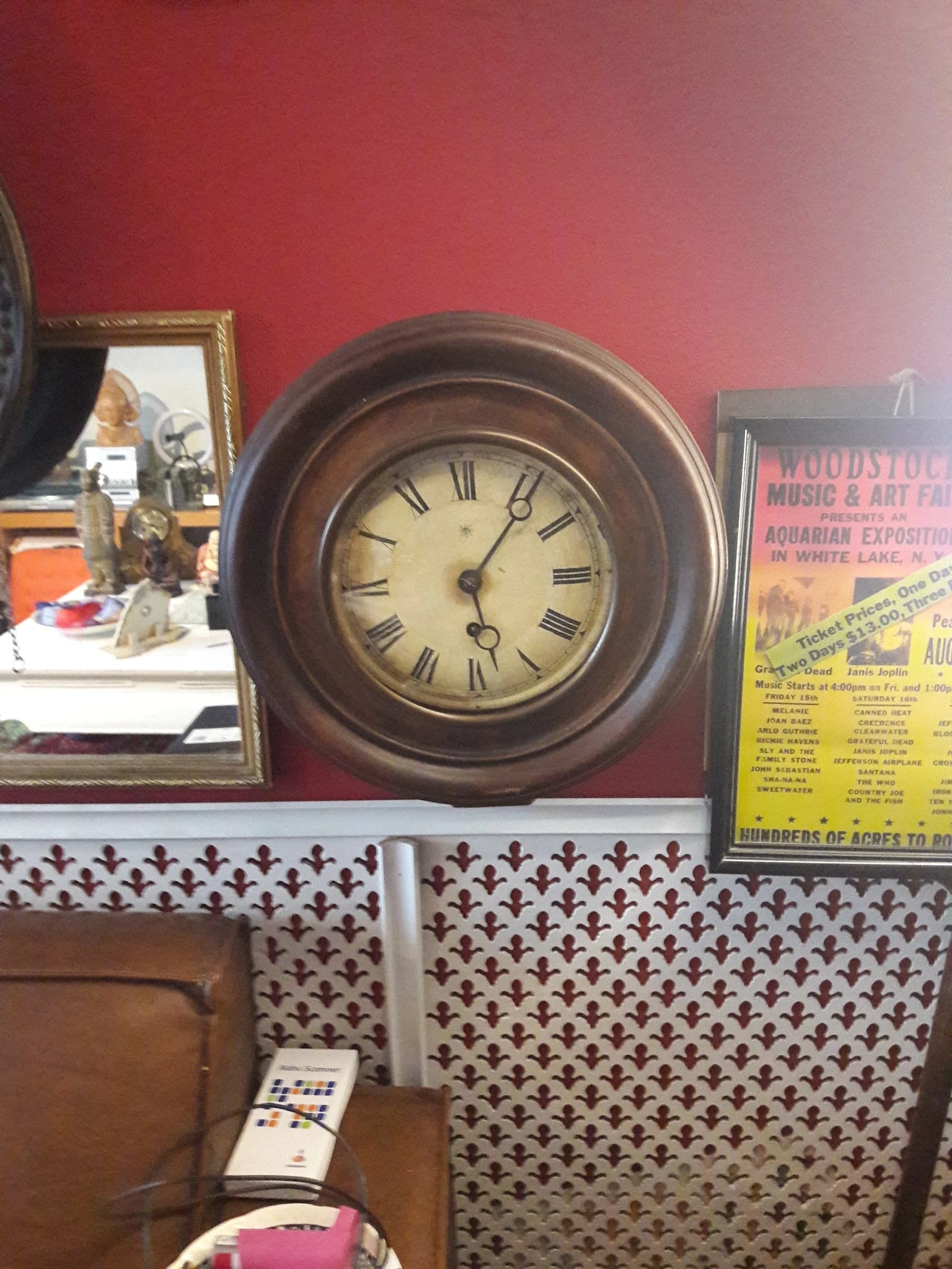 Vintage houten wandklok met Romeinse cijfers naast een gele Woodstock-festival poster, beide uitgestald in de winkel