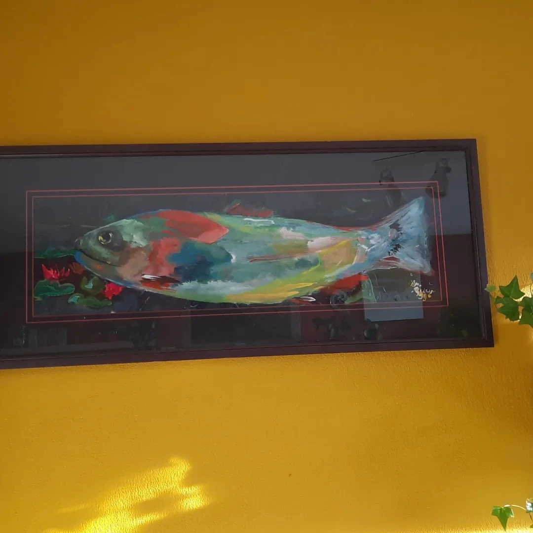 Ingelijste kunstwerk of decoratie van een gekleurde vis tegen gele muur