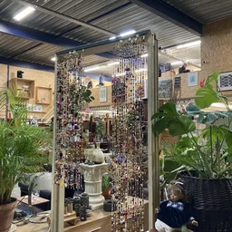 Binnenaanzicht van kringloopwinkel met plantenuitstalling, wanddecoratie en beaded gordijnen