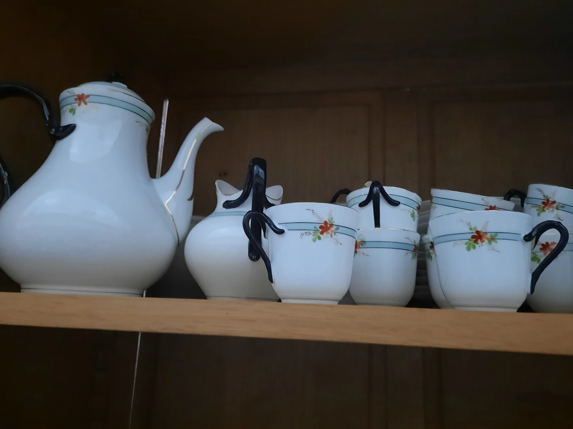 Wit porseleinen servies met bloemendecoratief motief: theepot en vier kopjes met zwarte handvaten op houten plank