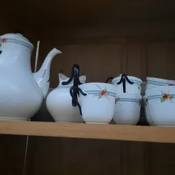Wit porseleinen servies met bloemendecoratief motief: theepot en vier kopjes met zwarte handvaten op houten plank