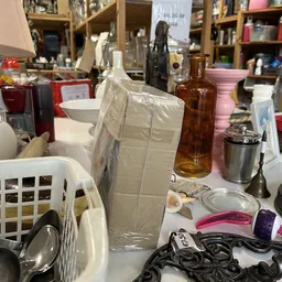 Tafel vol huishoudelijke spullen: plastic mand, glazen fles, metalen container, kunststof bakken en ander bric-à-brac
