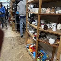 Houten stellingen met servies, borden, kommen en huishoudartikelen in de kringloopwinkel