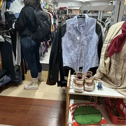 Uitgestalde tweedehands kleding en schoenen in een kringloopwinkel, met rekken met onder meer een gestreept vest en beige sch