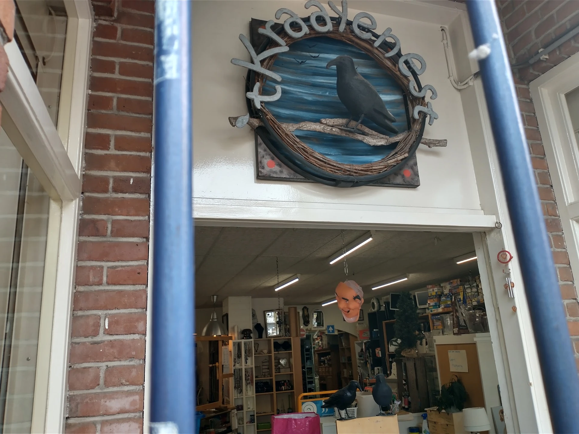 Winkelraam met blauw frame en decoratieve vis boven de ingang, man zichtbaar in winkelinterieur