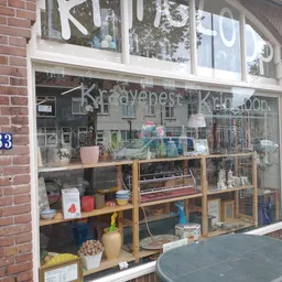 Winkelraam met vitrine van kringloopwinkel, witte kozijnen, nummerbord 583, diverse spullen zichtbaar