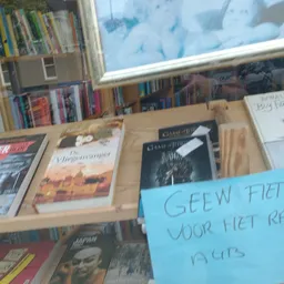 Boeken en dvd's uitgestald in dozen op een tafel met een blauw notitiebord